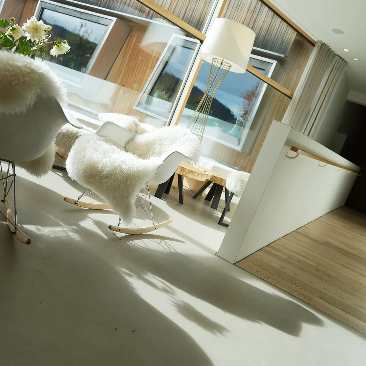 Gemütlicher Loungebereich im Tannenhof Sport & SPA mit modernen Schaukelstühlen, Schaffell und Blick in die Natur.