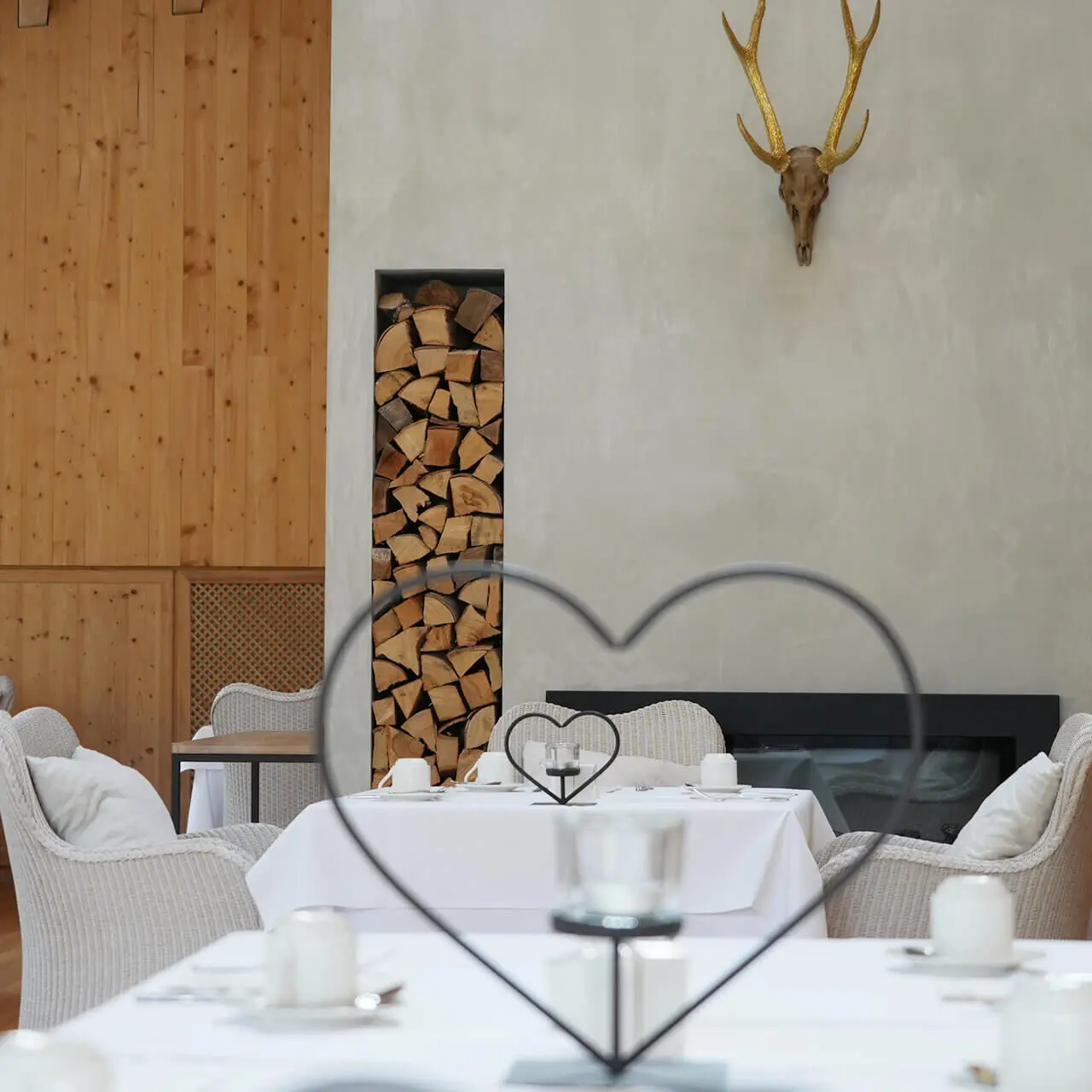 Gemütlicher Restaurantbereich im Tannenhof Sport & SPA mit Kamin, Holzstapel und alpiner Dekoration.