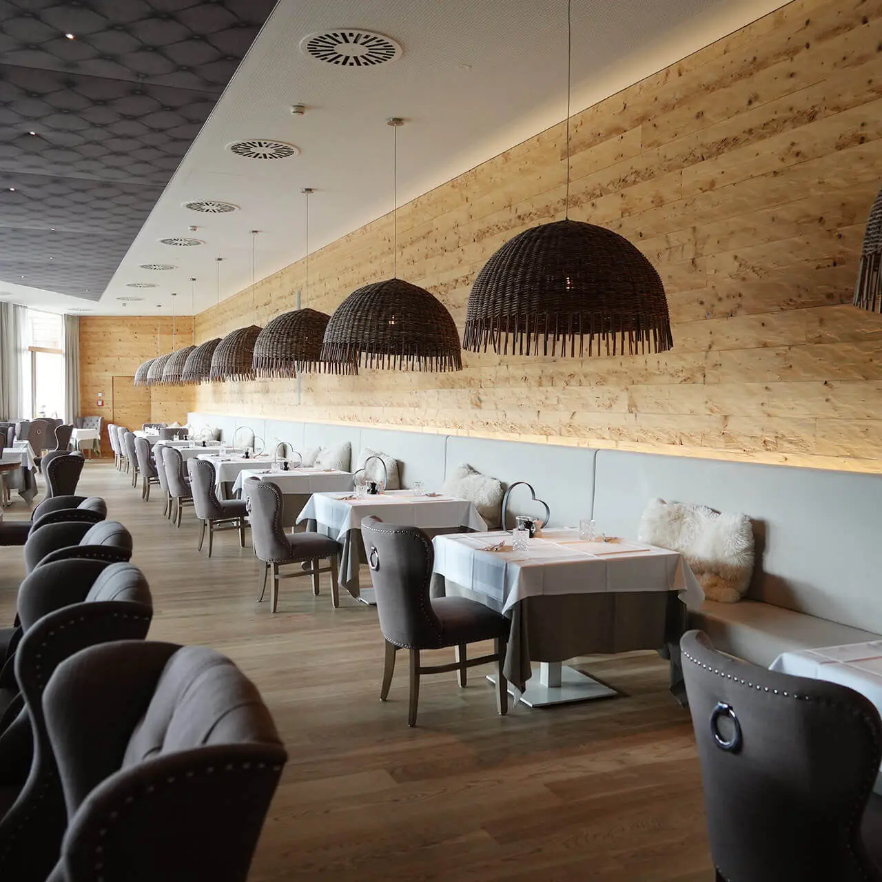 Elegantes Restaurant im Tannenhof Sport & SPA mit Holzwand, modernen Hängelampen und stilvollen Sitzgelegenheiten.