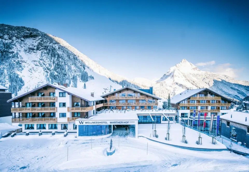 Aussenansicht des Wellnesshotel Warther Hof im Winter mit verschneiten Bergen und blauem Himmel.