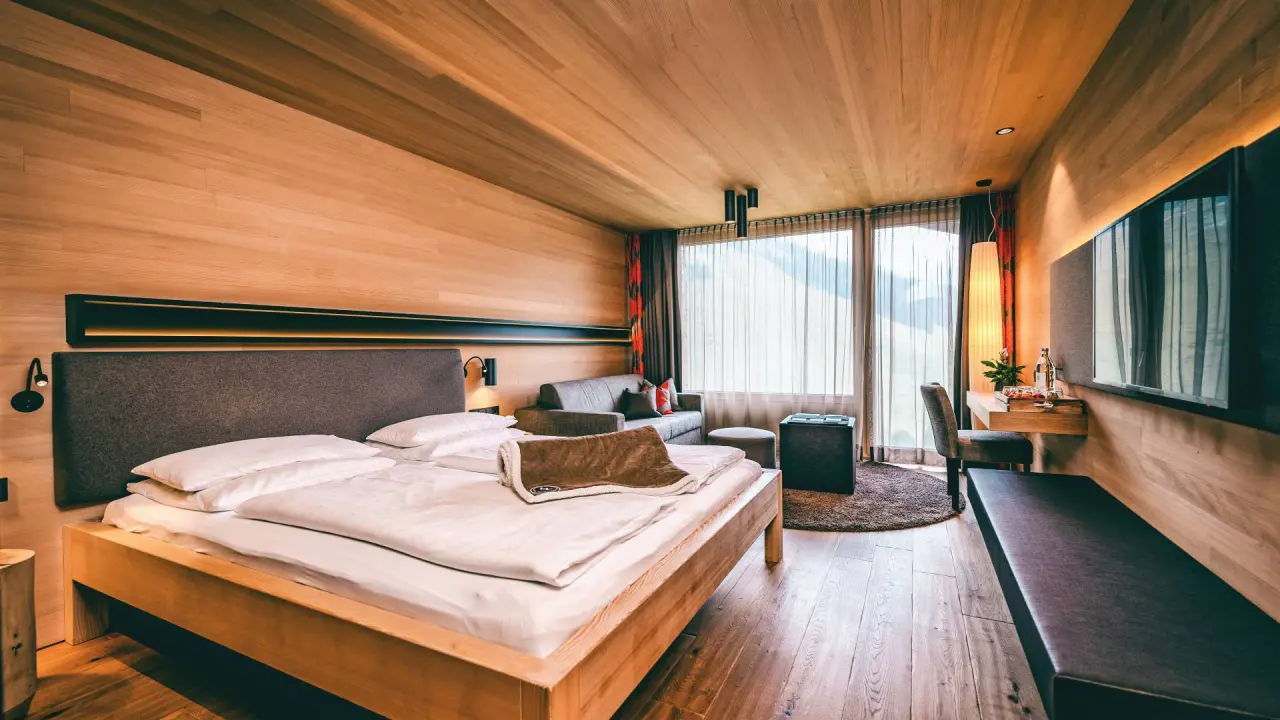 Modernes Doppelzimmer mit Holzelementen, Sofa und Bergblick im Wellnesshotel Warther Hof.