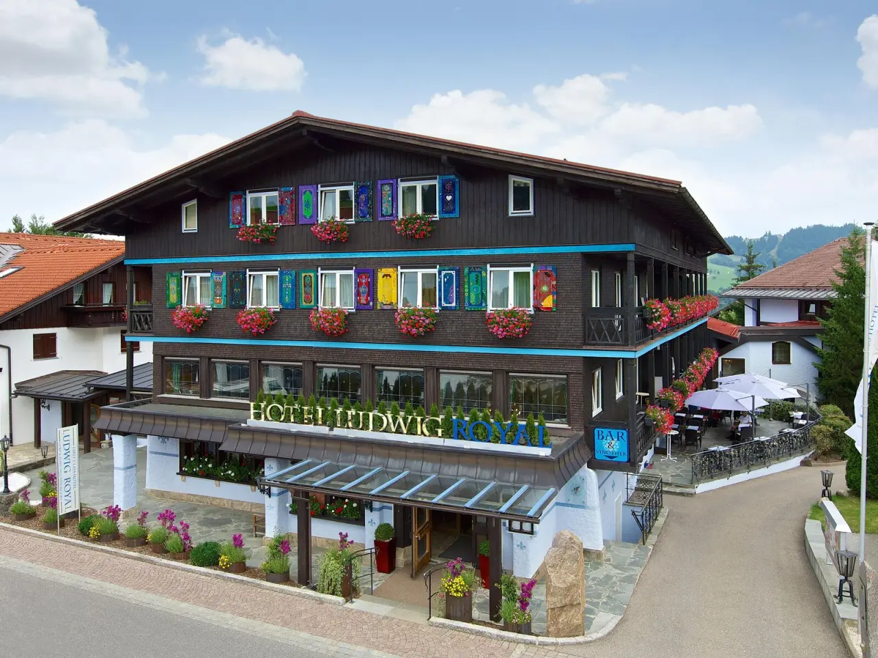 Aussenansicht des Golf- & Alpin Wellness Resort Hotel Ludwig Royal mit bunten Fensterläden und Blumenkästen.