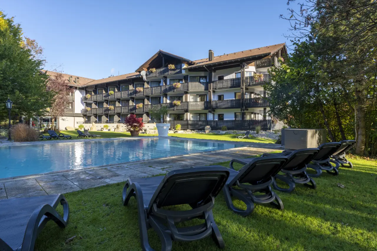 Sonniger Aussenpool mit Liegewiese und traditionellem Hotelgebäude im Golf- & Alpin Wellness Resort Hotel Ludwig Royal.