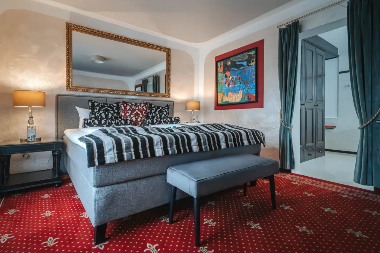 Komfortables Doppelzimmer mit rotem Teppich und Kunstwerk im Golf- & Alpin Wellness Resort Hotel Ludwig Royal.