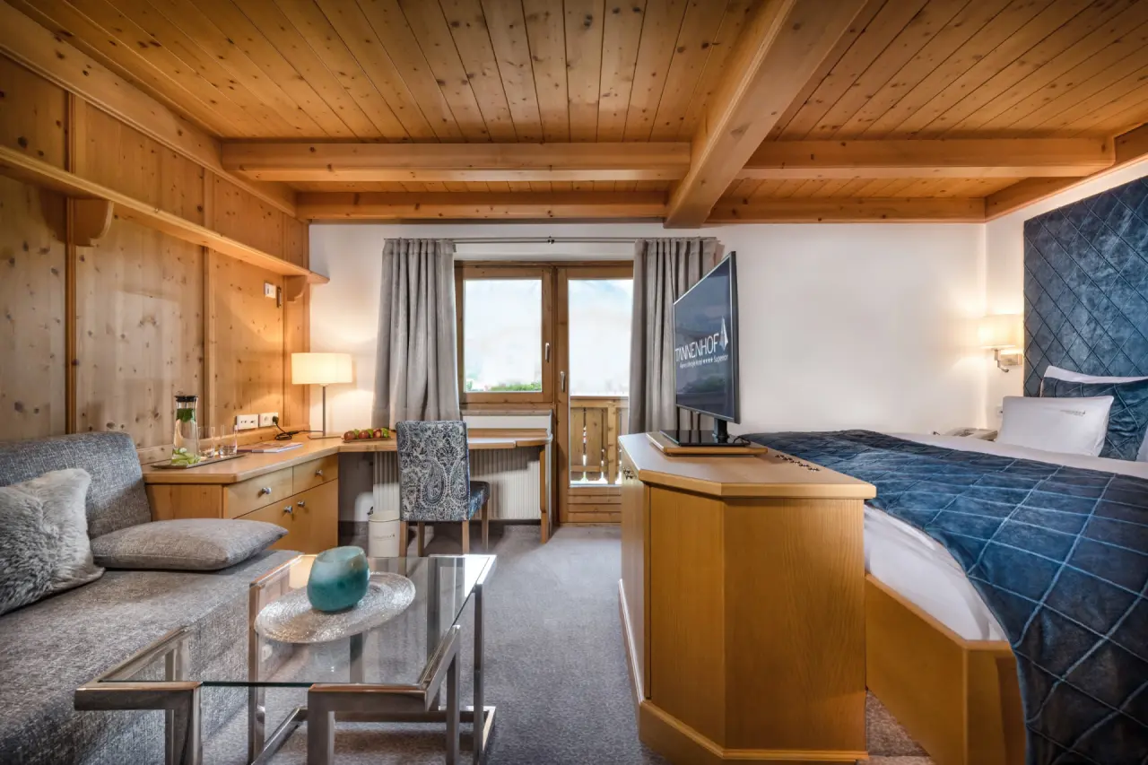 Geräumiges Hotelzimmer im alpinen Stil mit Holzelementen, Sofa, Balkon und Doppelbett im Alpines Lifestyle Hotel Tannenhof.