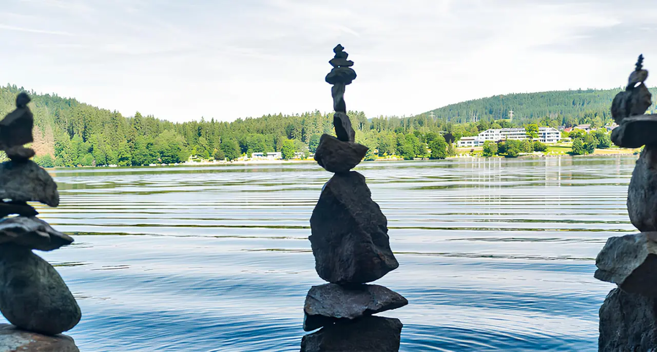 Gestapelte Steine am Titisee mit Blick auf Brugger's Hotelpark und die idyllische Schwarzwaldlandschaft.