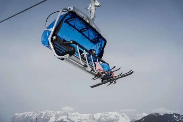 Skifahrer in einem blauen Sessellift mit verschneiten Bergen im Hintergrund, nahe dem Hotel Oberforsthof.
