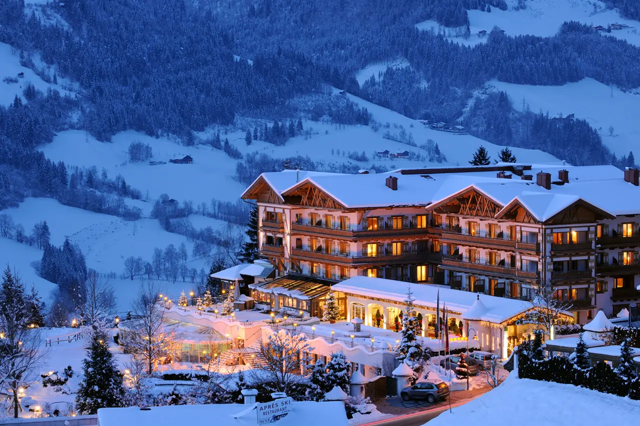 Hotel Oberforsthof im Winter: Beleuchtete Fassade und verschneite Alpenlandschaft bei Dämmerung.