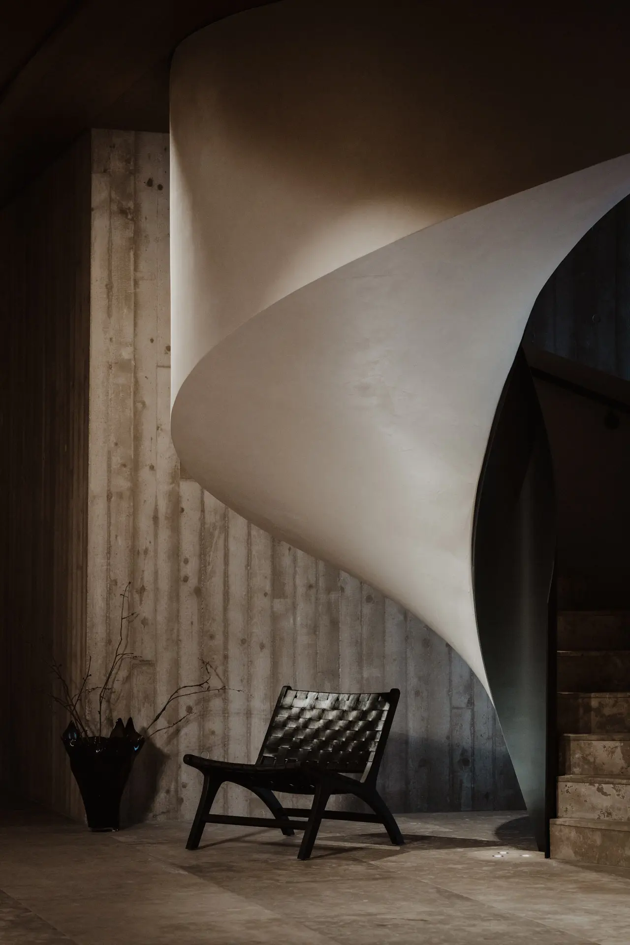 Moderne Architektur im Hotel Oberforsthof: Geschwungene Treppe und Design-Sessel vor Betonwand.