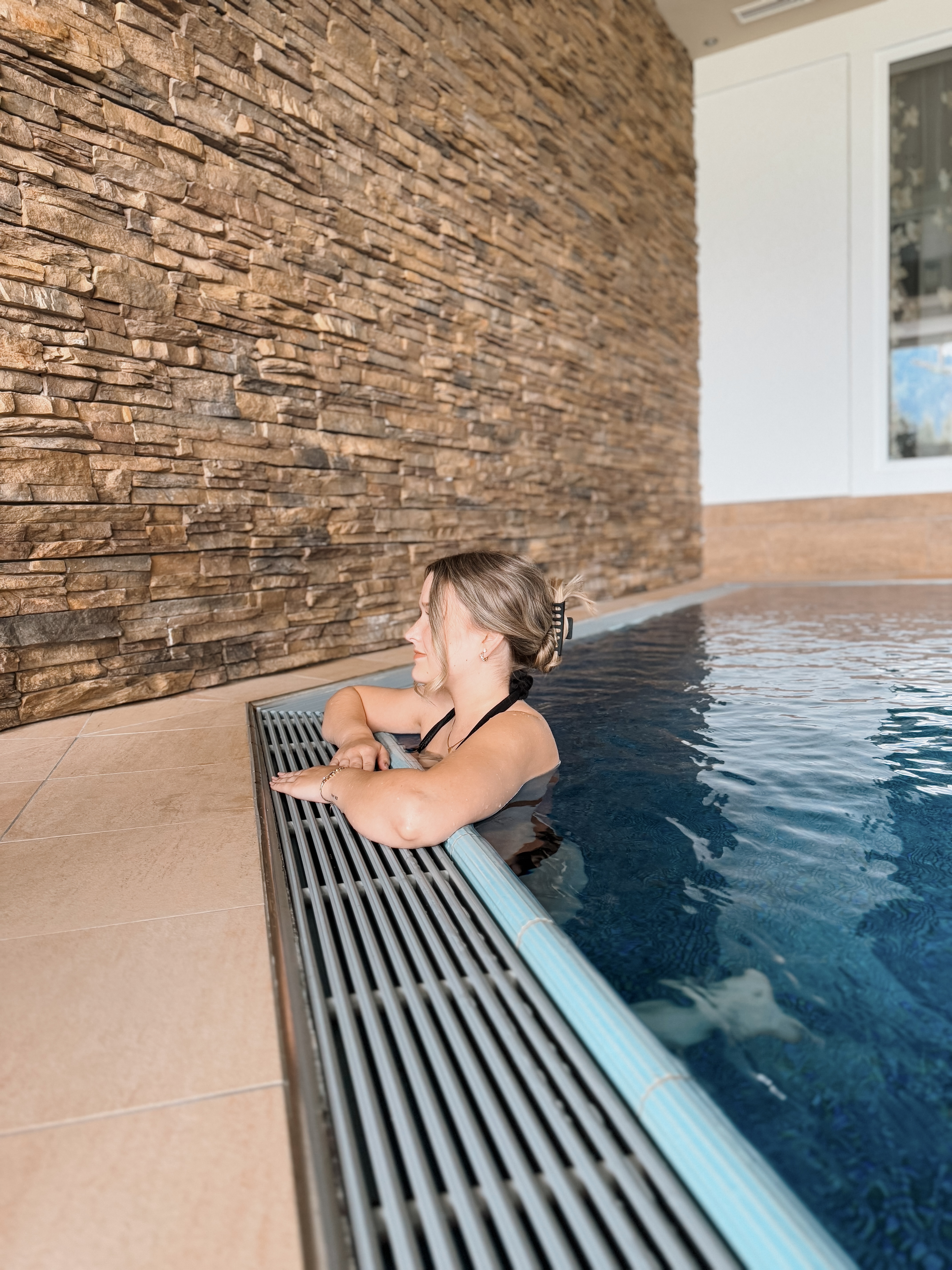 Alpinresort Schillerkopf in Bürserberg – Entspannte Frau im modernen Innenpool mit Steinwand | Wellnesshotel Vorarlberg