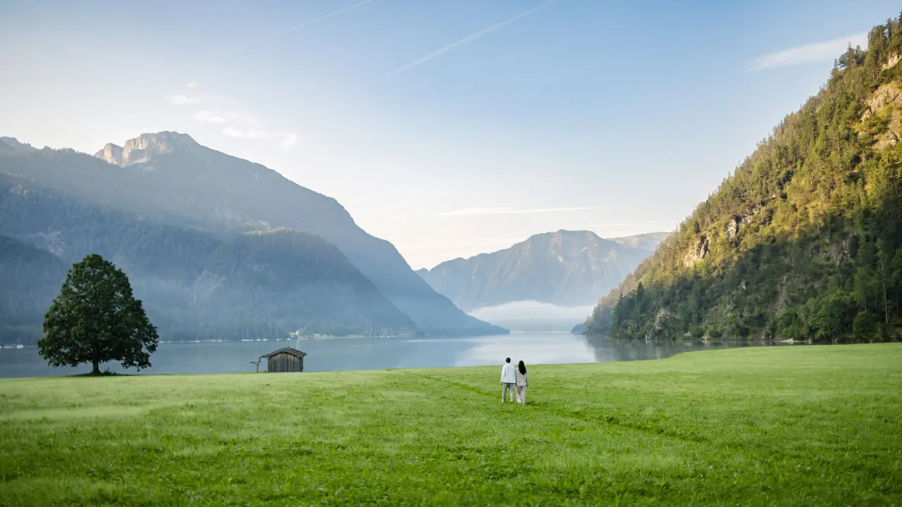 Romantischer Spaziergang eines Paares auf einer Wiese am Achensee mit Bergpanorama im Posthotel Achenkirch.