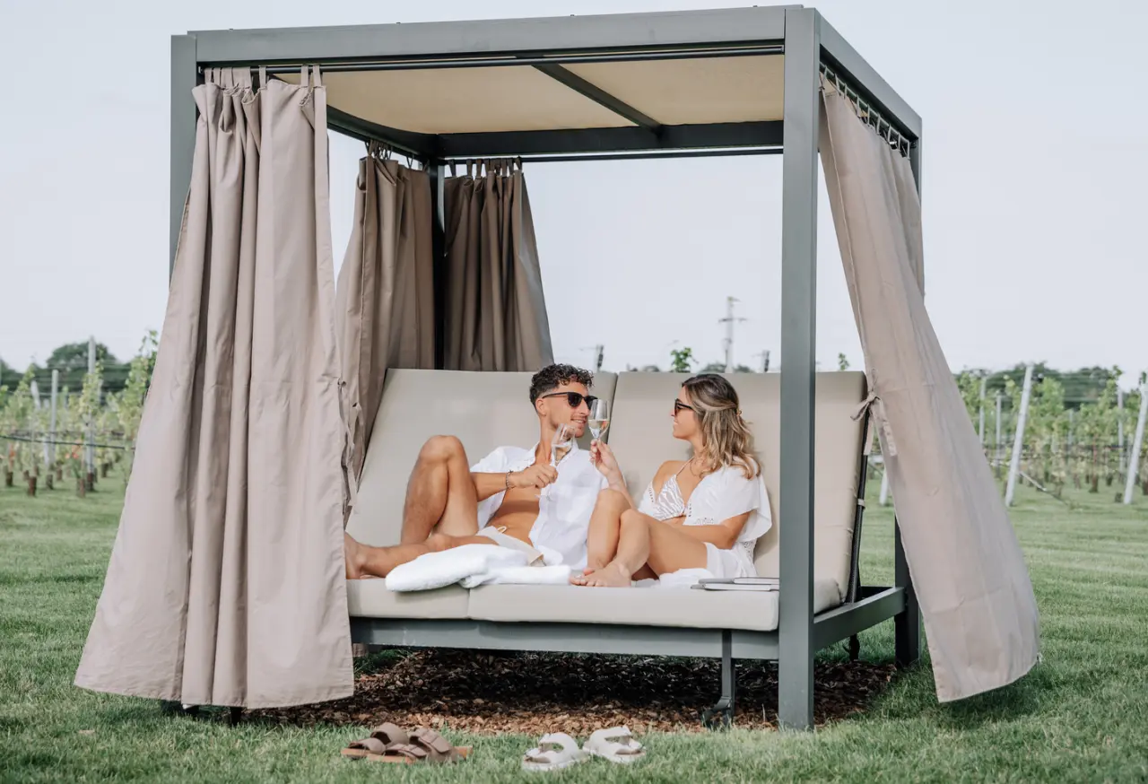 Paar entspannt mit Champagner auf einer luxuriösen Outdoor-Liege im Weinberg des Scheiblhofer The Resort.