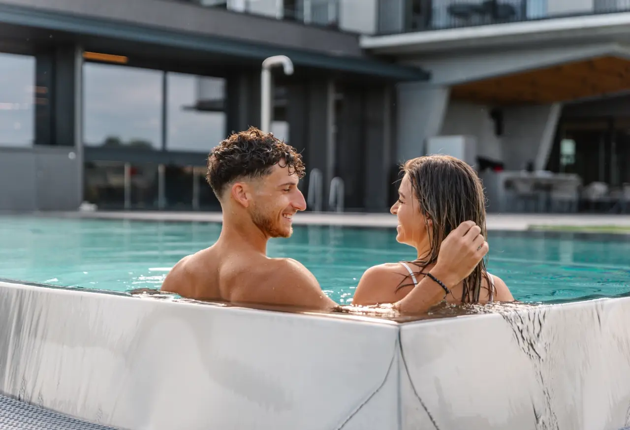 Glückliches Paar entspannt im modernen Außenpool des Scheiblhofer The Resort und genießt die Sonne.