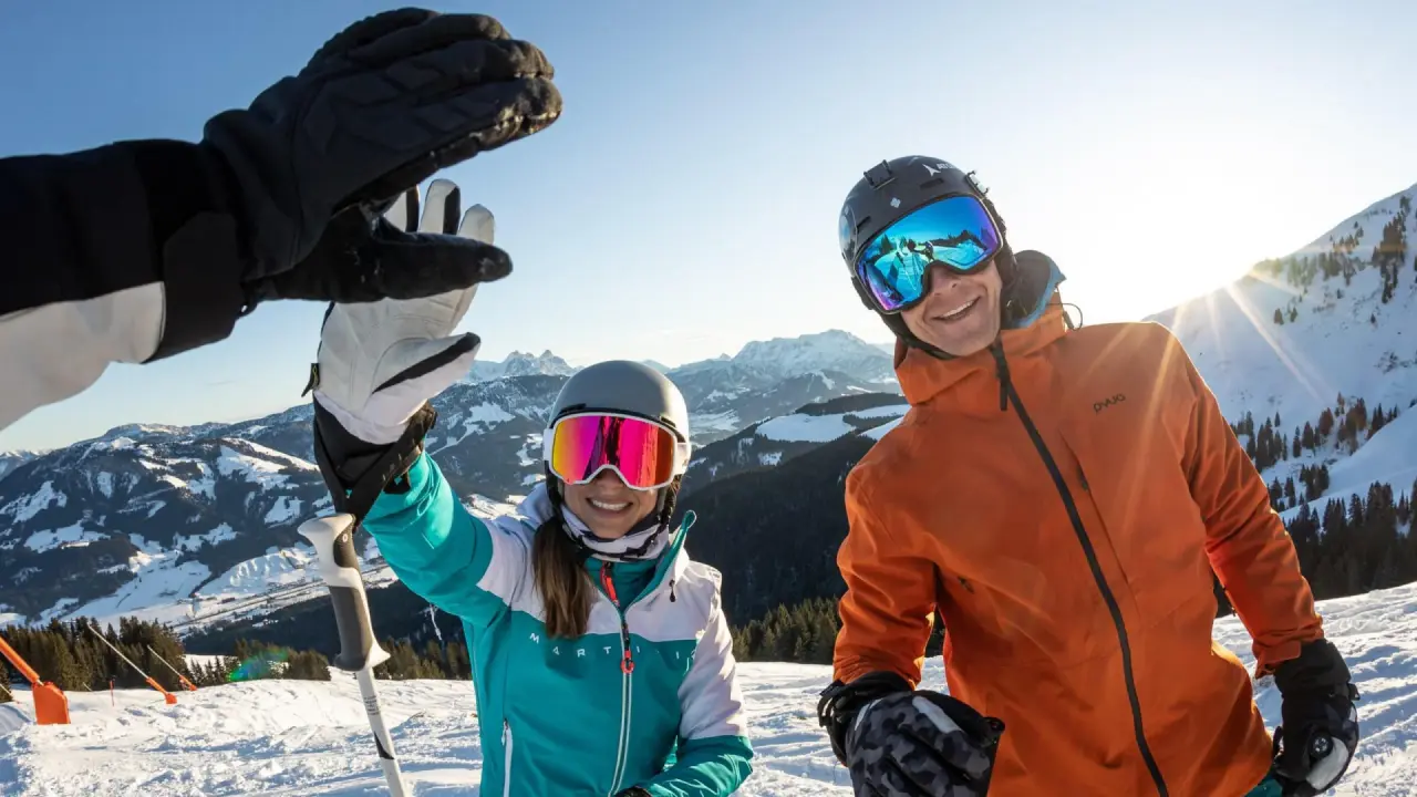 Fröhliche Skifahrer auf sonniger Skipiste mit Alpenpanorama, ideal für den Winterurlaub im Vitalhotel Berghof.