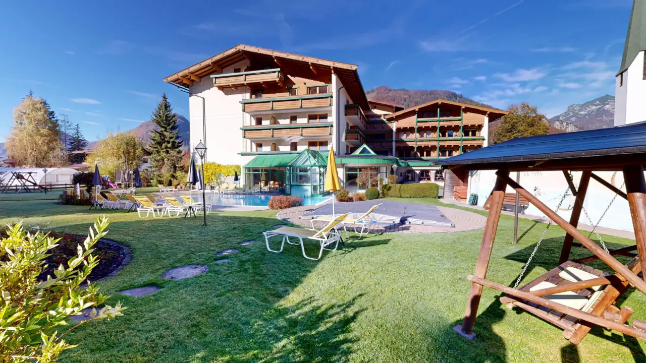 Aussenansicht des Vitalhotel Berghof mit Garten, Poolbereich und Alpenpanorama unter blauem Himmel.