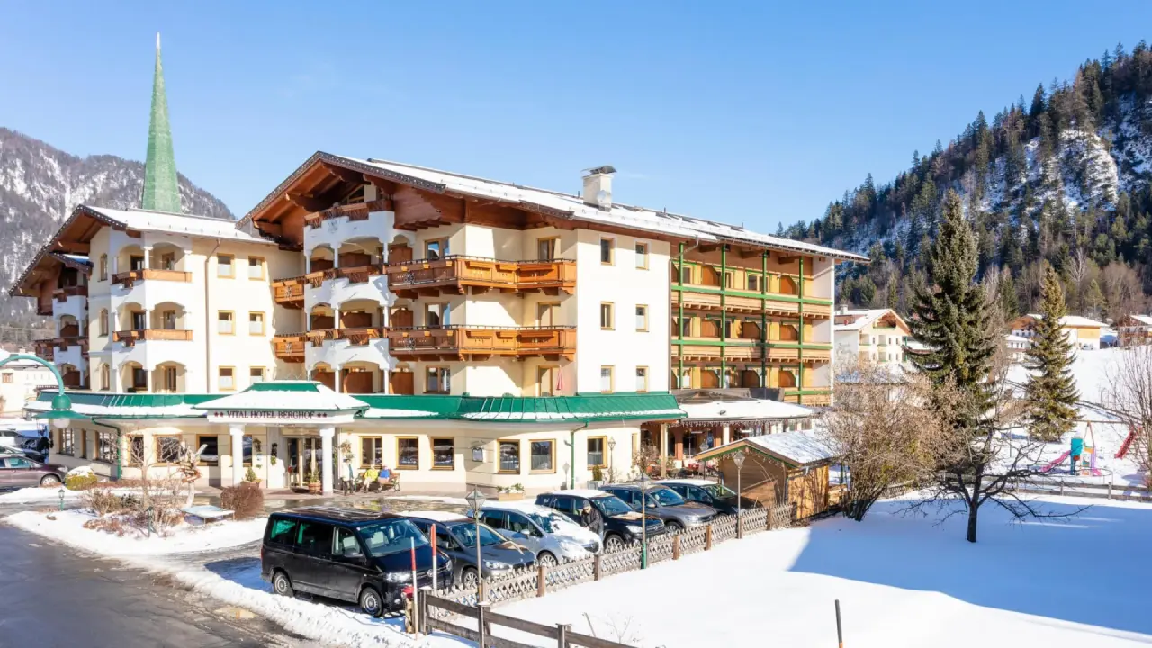 Aussenansicht des Vitalhotel Berghof im Winter mit schneebedeckten Bergen und blauem Himmel. Traditionelle Architektur in alpiner Landschaft.