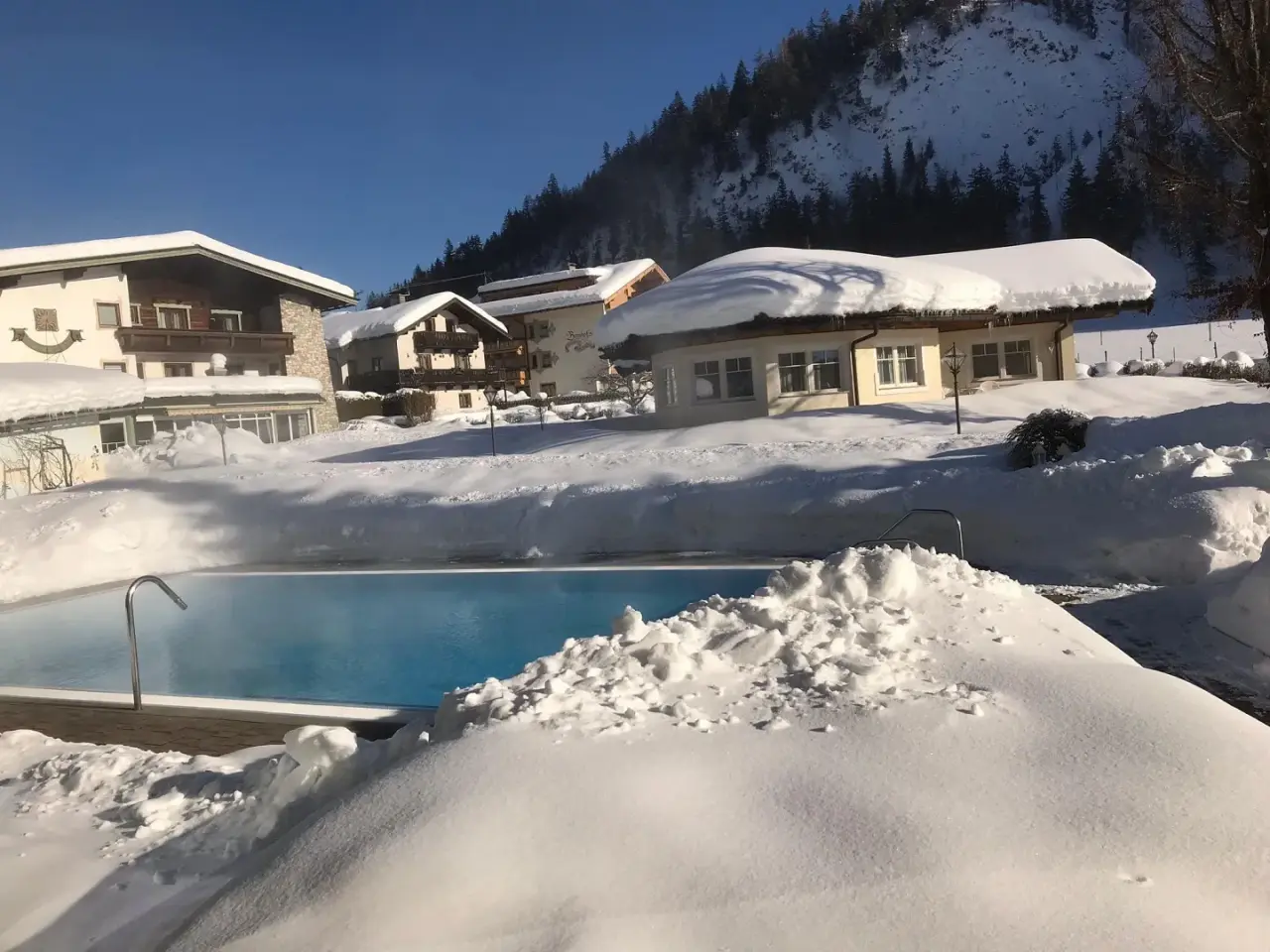 Beheizter Aussenpool im Schnee des Vitalhotel Berghof mit verschneiter Berglandschaft und Hotelgebäuden im Hintergrund.