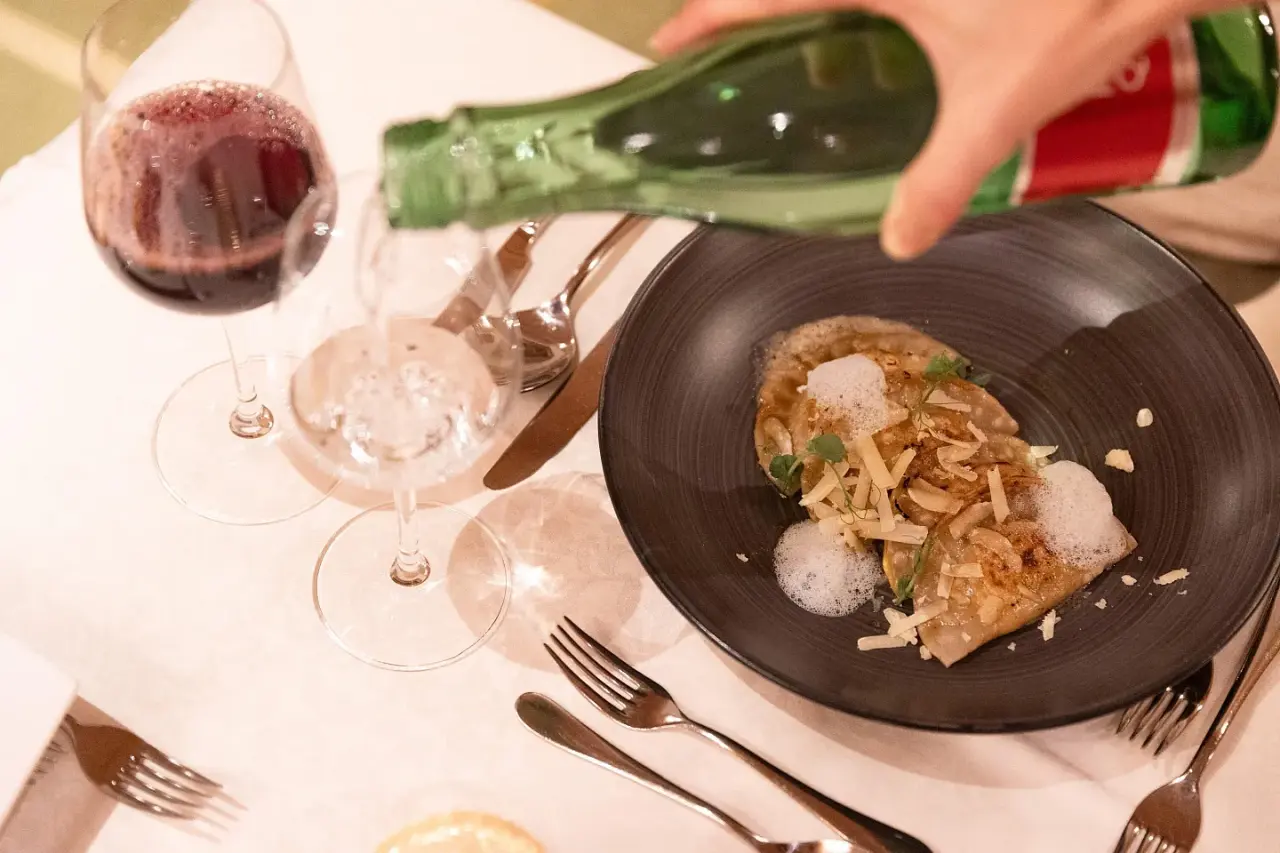 Gourmetgericht mit Wasser und Rotwein am elegant gedeckten Tisch im Restaurant des Vitalhotel Berghof.