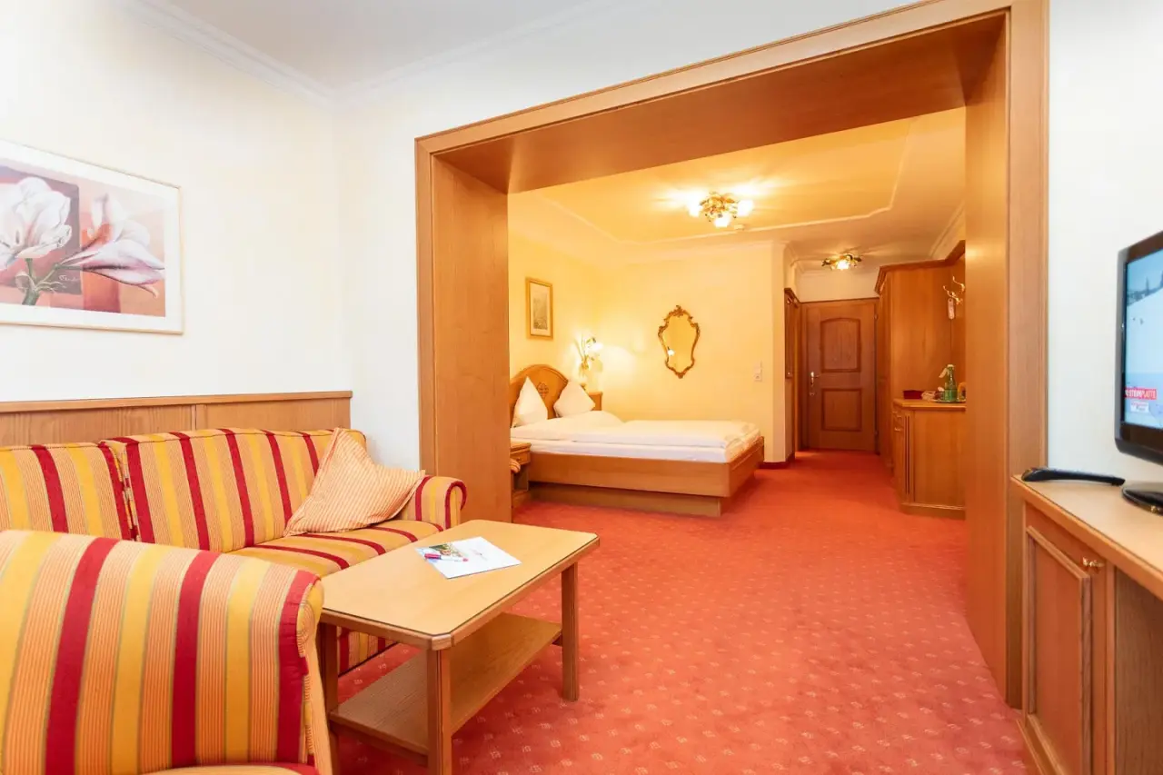 Gemütliche Suite im Vitalhotel Berghof mit Wohnbereich und Schlafzimmer, ausgestattet mit traditionellen Möbeln.