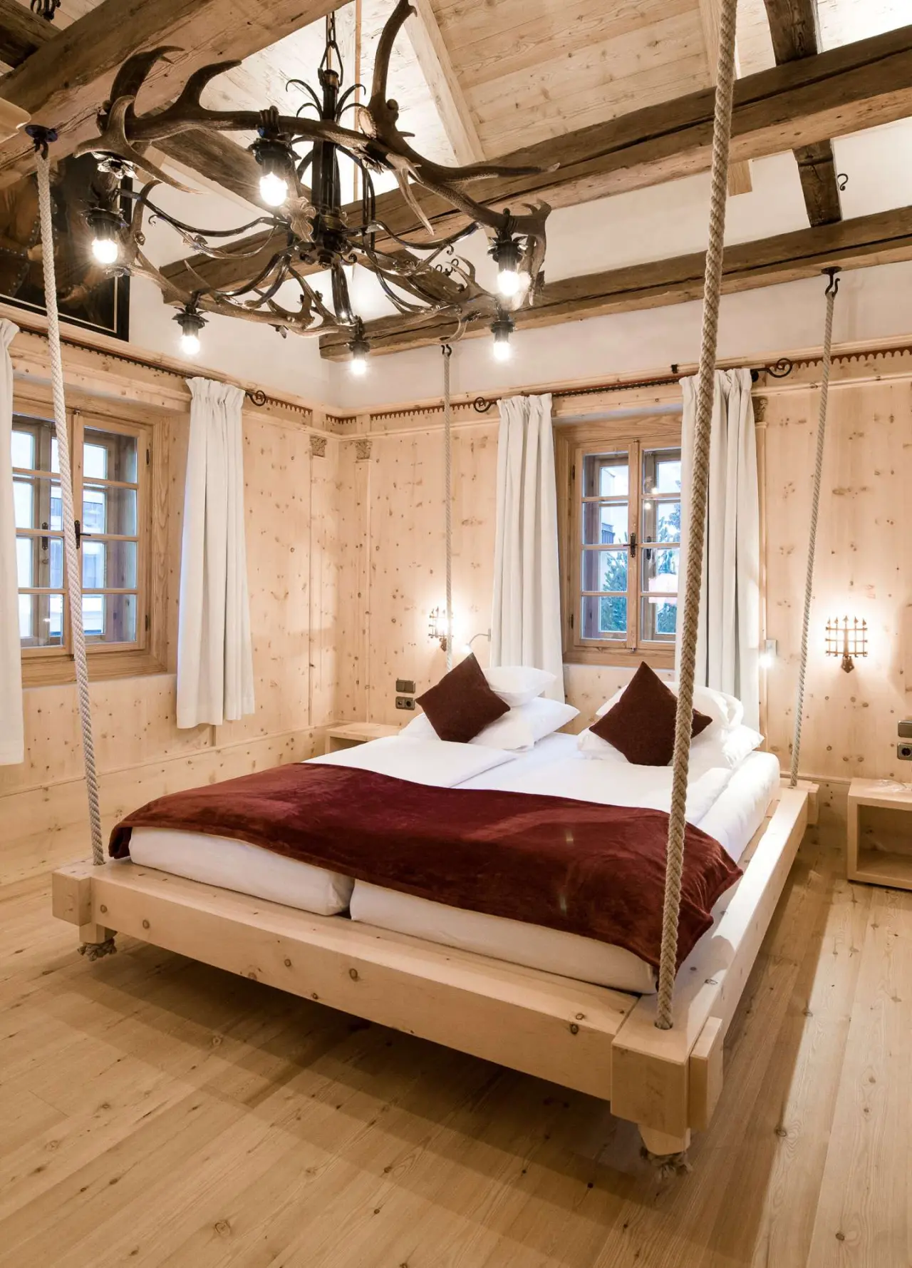 Einzigartiges Hotelzimmer im Hotel Norica mit schwebendem Holzbett, rustikalem Interieur und Geweih-Kronleuchter.