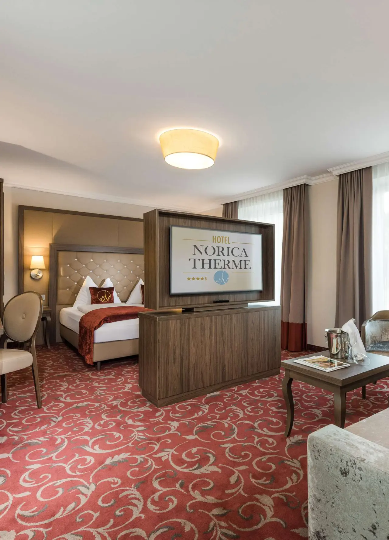 Komfortables Doppelzimmer im Hotel Norica Therme mit großem Bett, Sitzbereich und Fernseher.