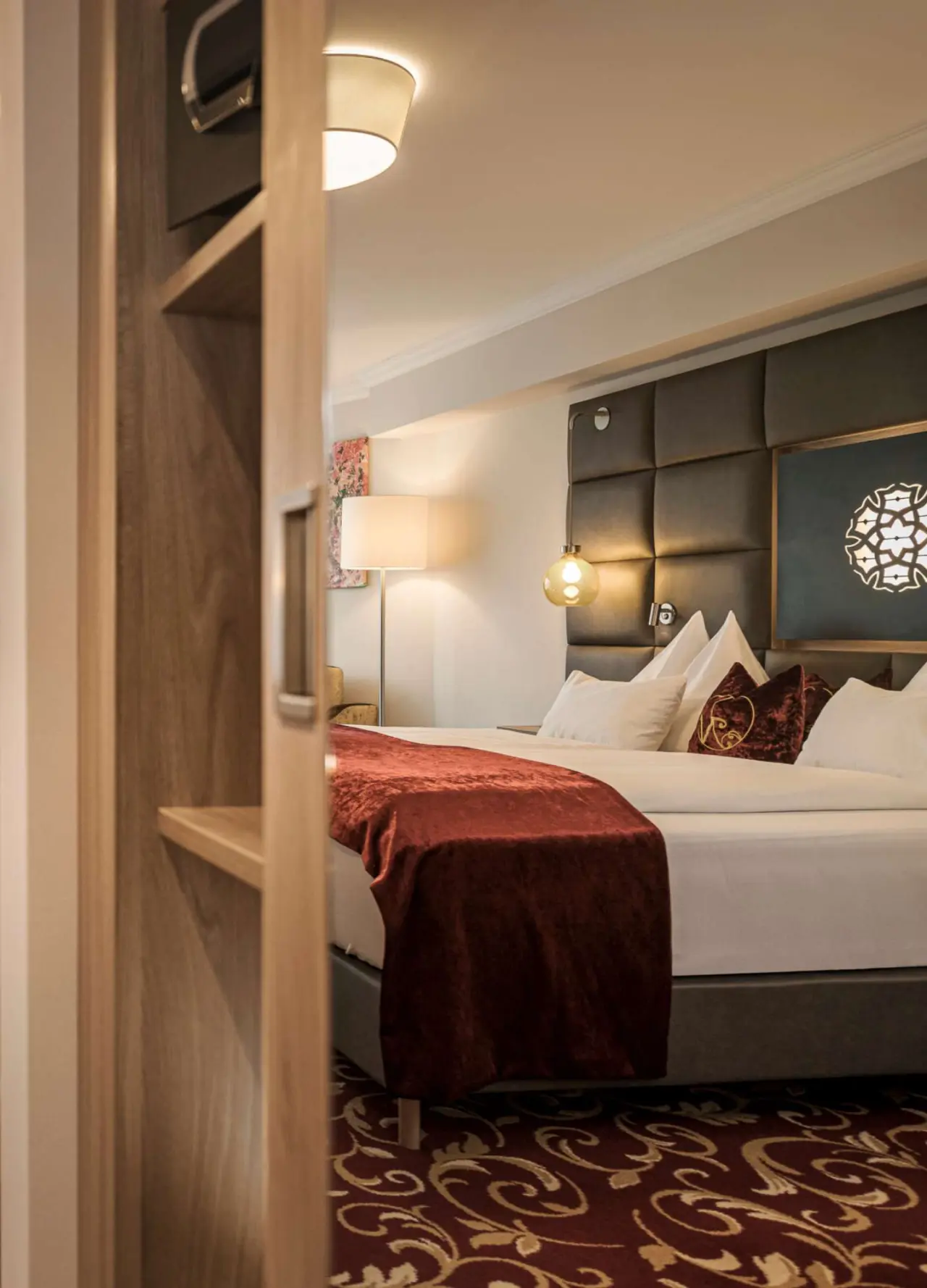 Elegantes Doppelzimmer im Hotel Norica mit luxuriösem Bett, rotem Überwurf und stimmungsvoller Beleuchtung für erholsamen Schlaf.
