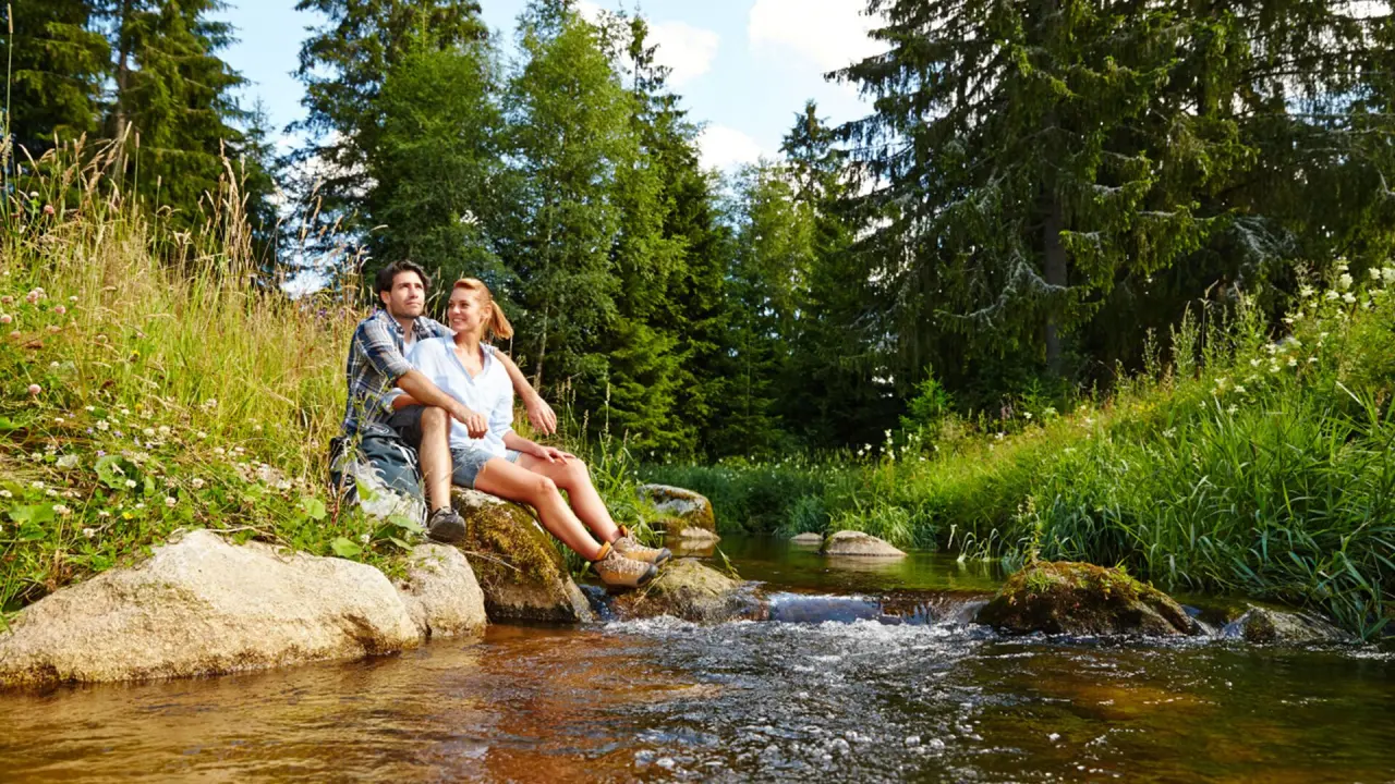 Paar entspannt am idyllischen Bachlauf im Wald, umgeben von Natur. Perfekt für Wanderungen und Erholung nahe Parkhotel Adler.