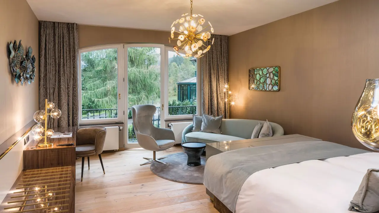 Luxuriöses Hotelzimmer im Parkhotel Adler mit elegantem Sitzbereich, großem Bett und Blick ins Grüne.