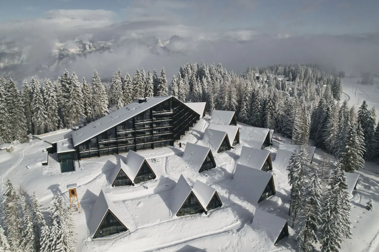 TRIFORÊT alpin.resort im Winter: Moderne Architektur und Chalets inmitten verschneiter Alpenlandschaft und Tannenwäldern.