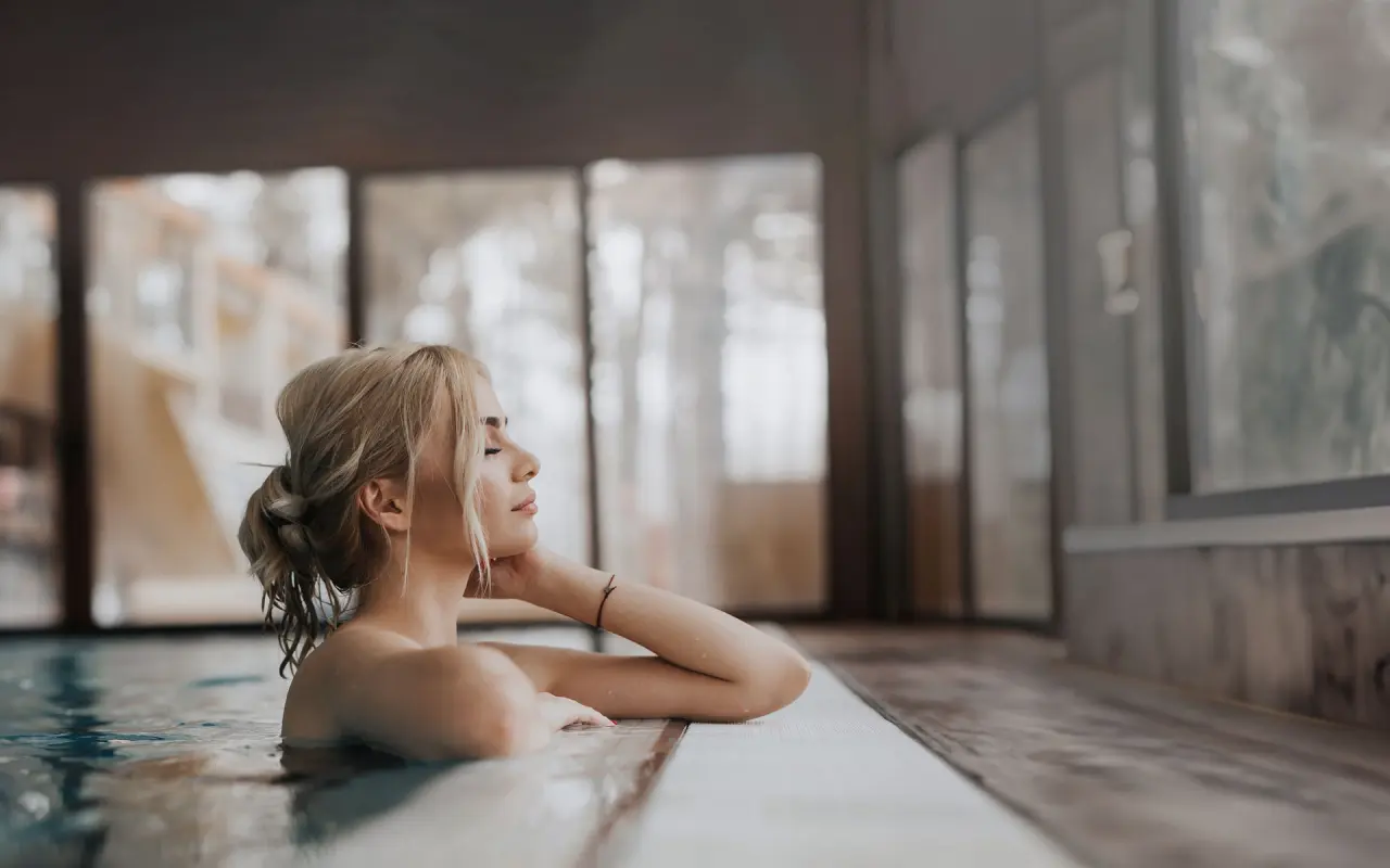 Entspannte Frau genießt das warme Wasser im Innenpool des TRIFORÊT alpin.resort. Perfekt für Wellness und Erholung.