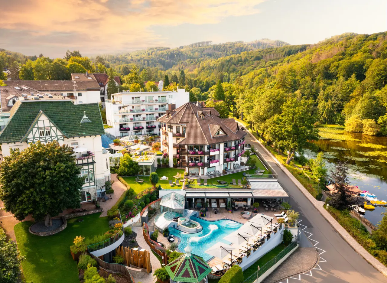 Panoramablick auf das Hotel Romantischer Winkel - RoLigio® & Wellness Resort mit Poolanlage, See und grüner Landschaft.