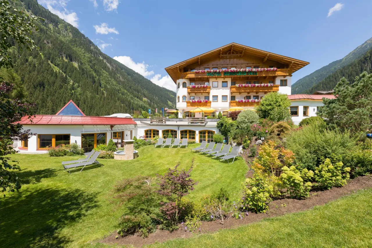 Aussenansicht des Aktiv- & Vitalhotel Bergcristall mit sonnigem Garten, Liegewiese und beeindruckendem Bergpanorama.
