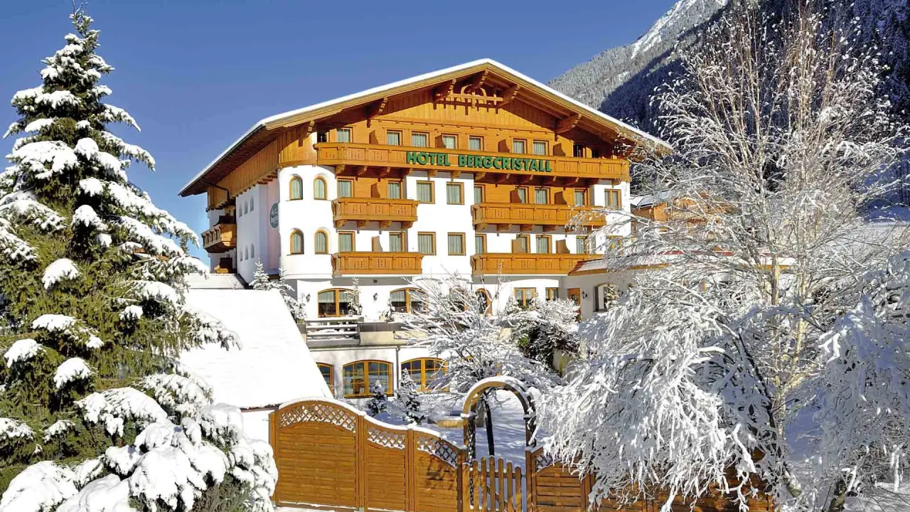 Aktiv- & Vitalhotel Bergcristall im Winter, umgeben von verschneiten Bäumen und Bergen unter blauem Himmel.