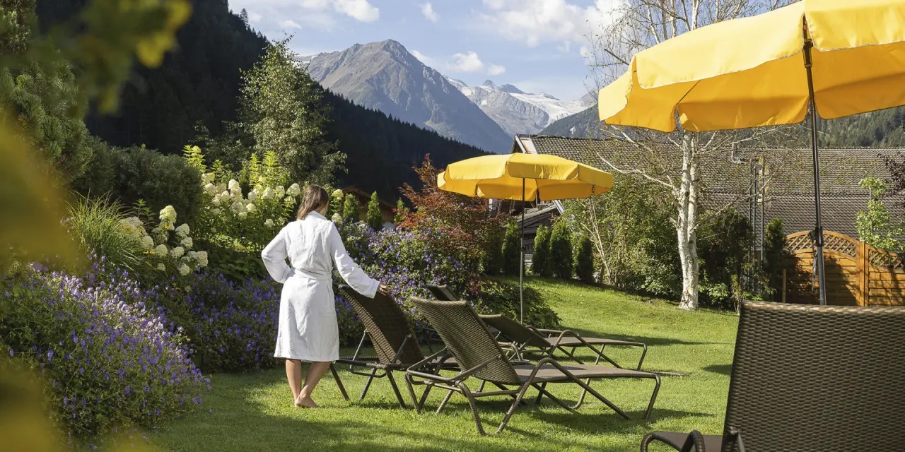 Gast im Bademantel entspannt im Hotelgarten mit Liegestühlen und Blick auf die Berge im Aktiv- & Vitalhotel Bergcristall.