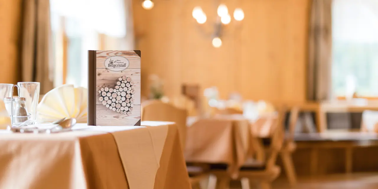 Gedeckter Tisch mit Speisekarte im Restaurant des Aktiv- & Vitalhotel Bergcristall. Rustikales Holzdesign und warme Farben.
