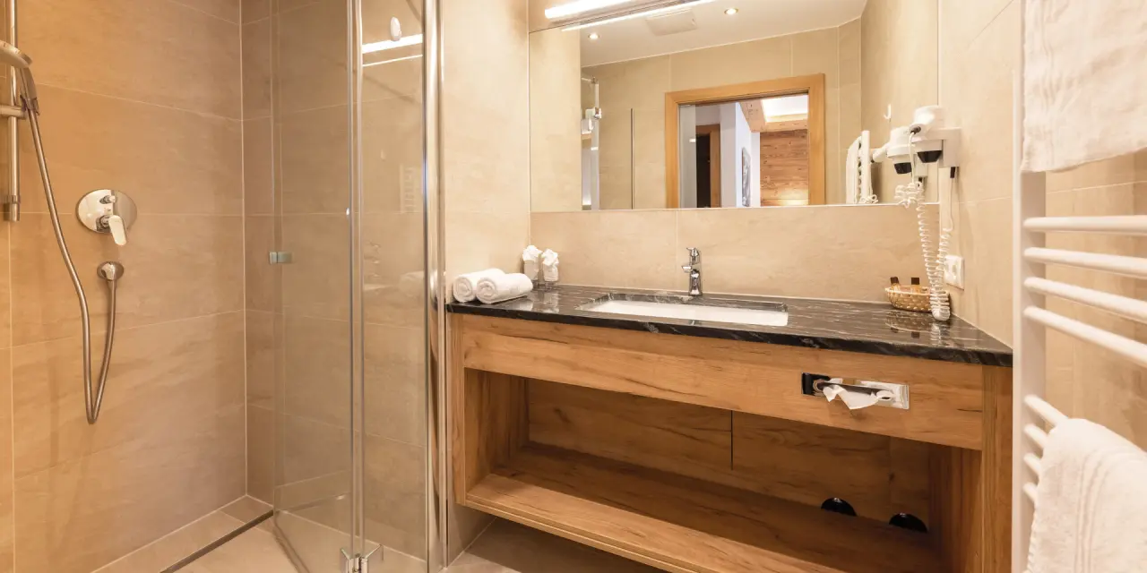 Modernes Badezimmer mit begehbarer Dusche und Holzwaschtisch im Aktiv- & Vitalhotel Bergcristall.