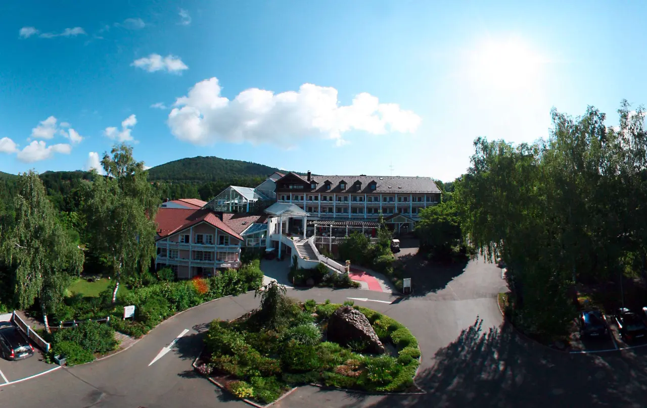 Weitwinkel-Aussenansicht des Hotel Wutzschleife mit Zufahrt und grüner Naturkulisse unter blauem Himmel.