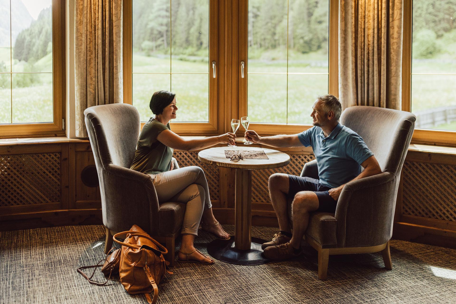 Hotel Weisseespitze in Kaunertal – Paar genießt Sekt in gemütlicher Sitzecke mit Bergblick | Wellnesshotel Tirol