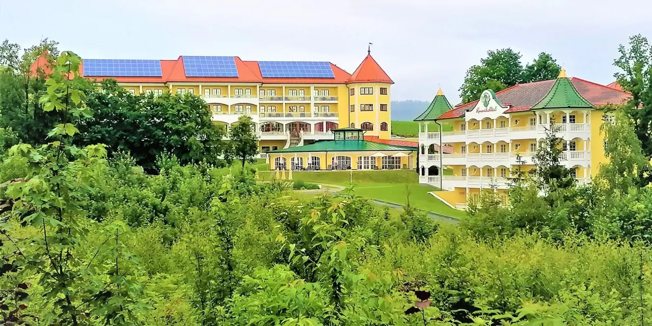 Aussenansicht des Parkschlössl zu Thyrnau mit gelben Fassaden, roten Dächern und grüner Umgebung, umgeben von Bäumen.