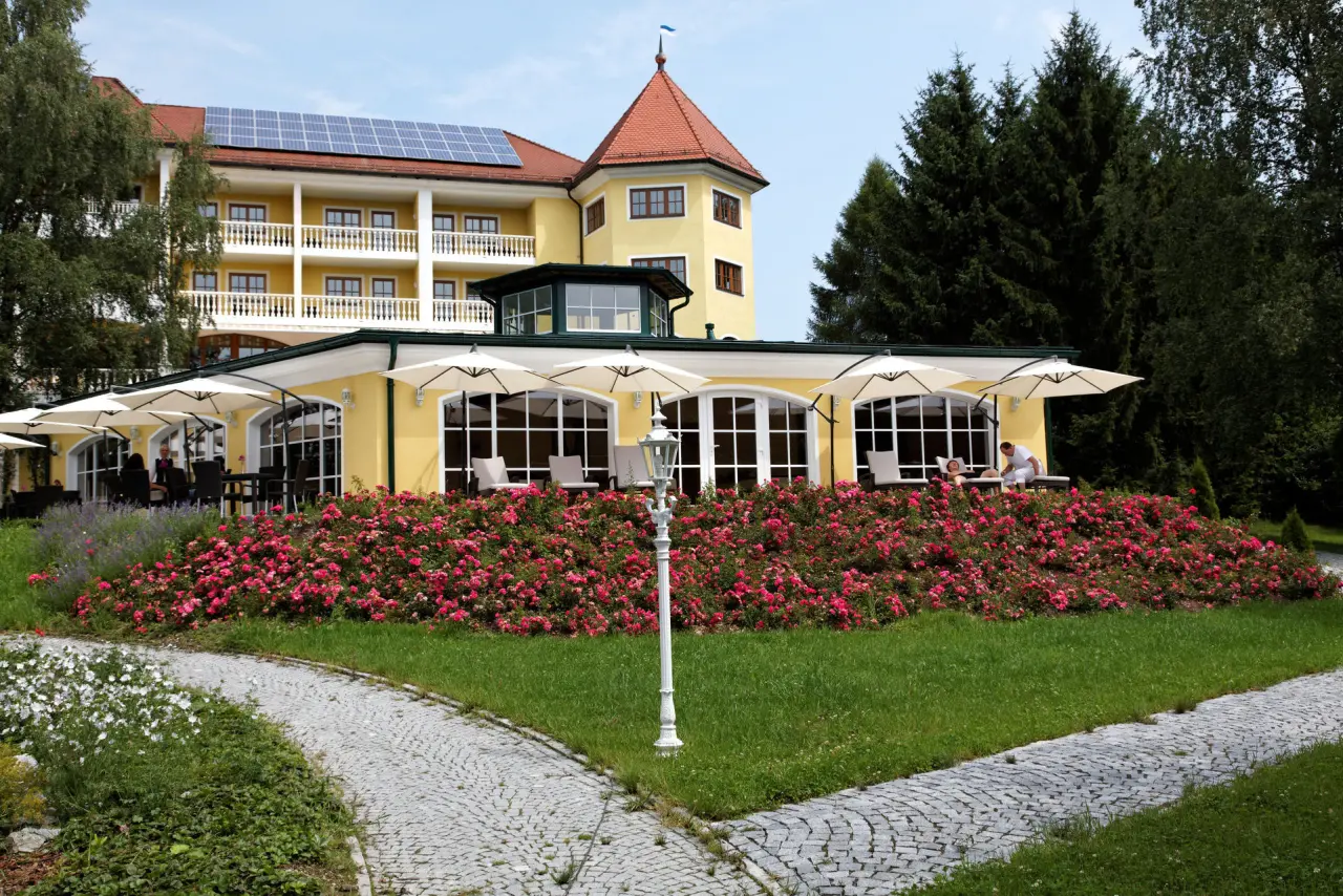 Aussenansicht des Parkschlössl zu Thyrnau mit gelber Fassade, Turm, Sonnenterrasse und blühenden Rosen im Garten.