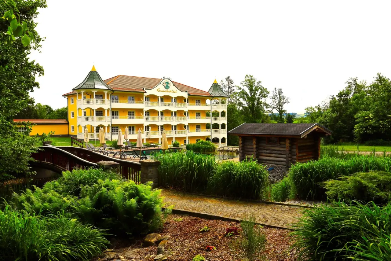 Parkschlössl zu Thyrnau: Malerisches gelbes Hotelgebäude mit Türmchen, umgeben von einem grünen Garten mit Pool und Holzbrücke.
