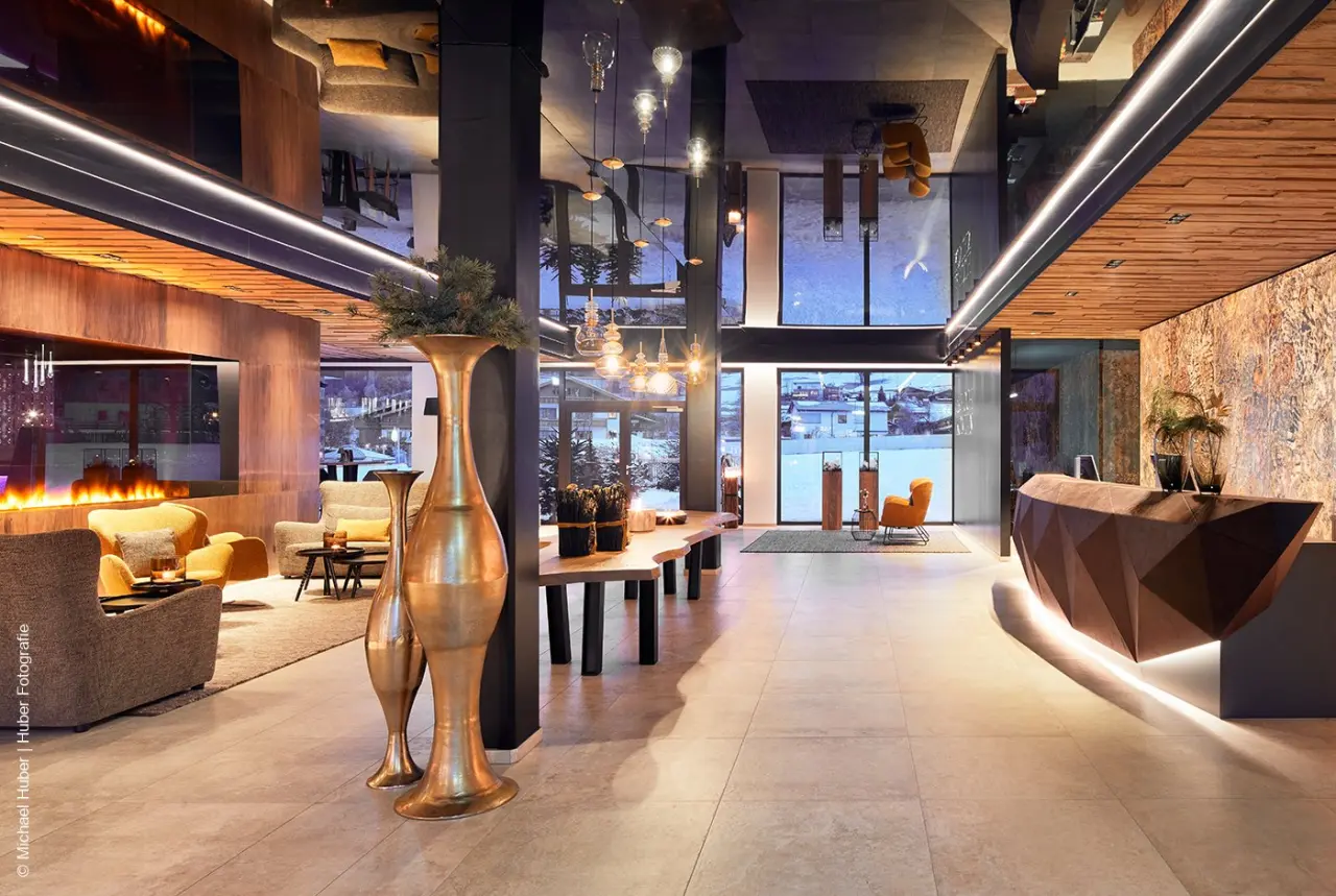 Moderne und luxuriöse Hotellobby des die HOCHKÖNIGIN - Mountain Resort mit Kamin, Rezeption und Blick auf die Winterlandschaft.