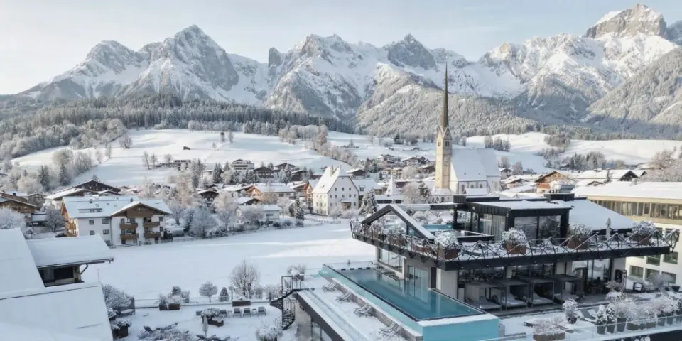 Beheizter Infinity Pool mit Blick auf das verschneite Bergpanorama und das Dorf im die HOCHKÖNIGIN - Mountain Resort.