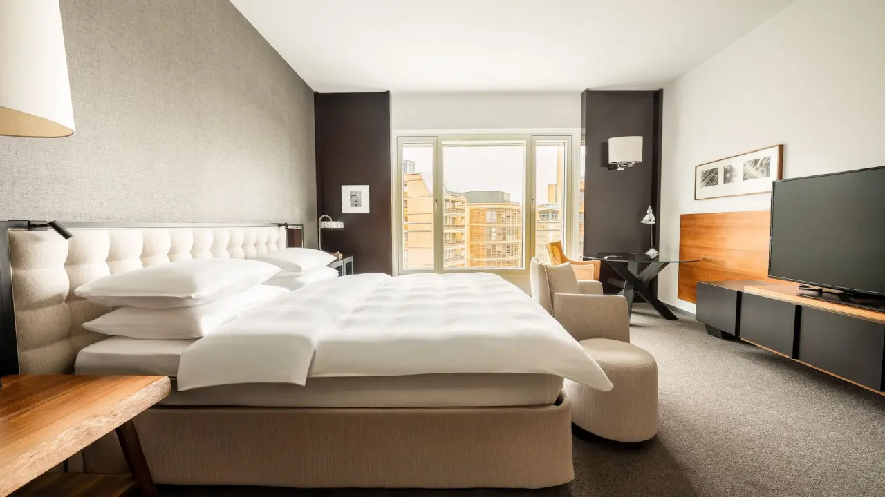 Modernes Hotelzimmer im Grand Hyatt Berlin mit großem Bett, Sitzbereich und Stadtblick aus dem Fenster.