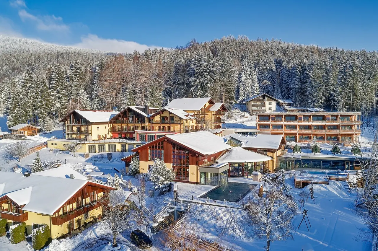 Wellnesshotel Riedlberg im Winter: Hotelanlage mit Aussenpool und verschneiter Waldlandschaft unter blauem Himmel.