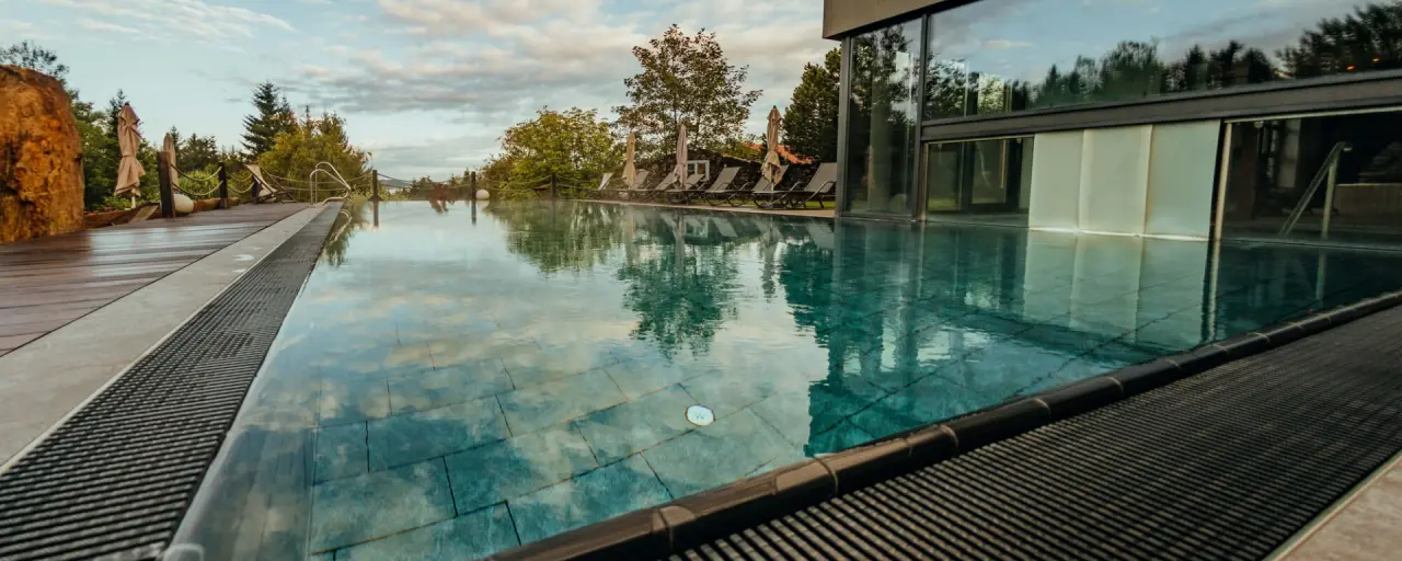 Infinity-Außenpool mit Holzdeck und Liegen im Wellnesshotel Riedlberg, umgeben von Natur und Bäumen.