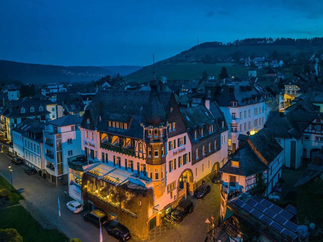 Romantik Jugendstilhotel Bellevue bei Abenddämmerung, beleuchtet in malerischer Stadtkulisse mit Weinbergen im Hintergrund.