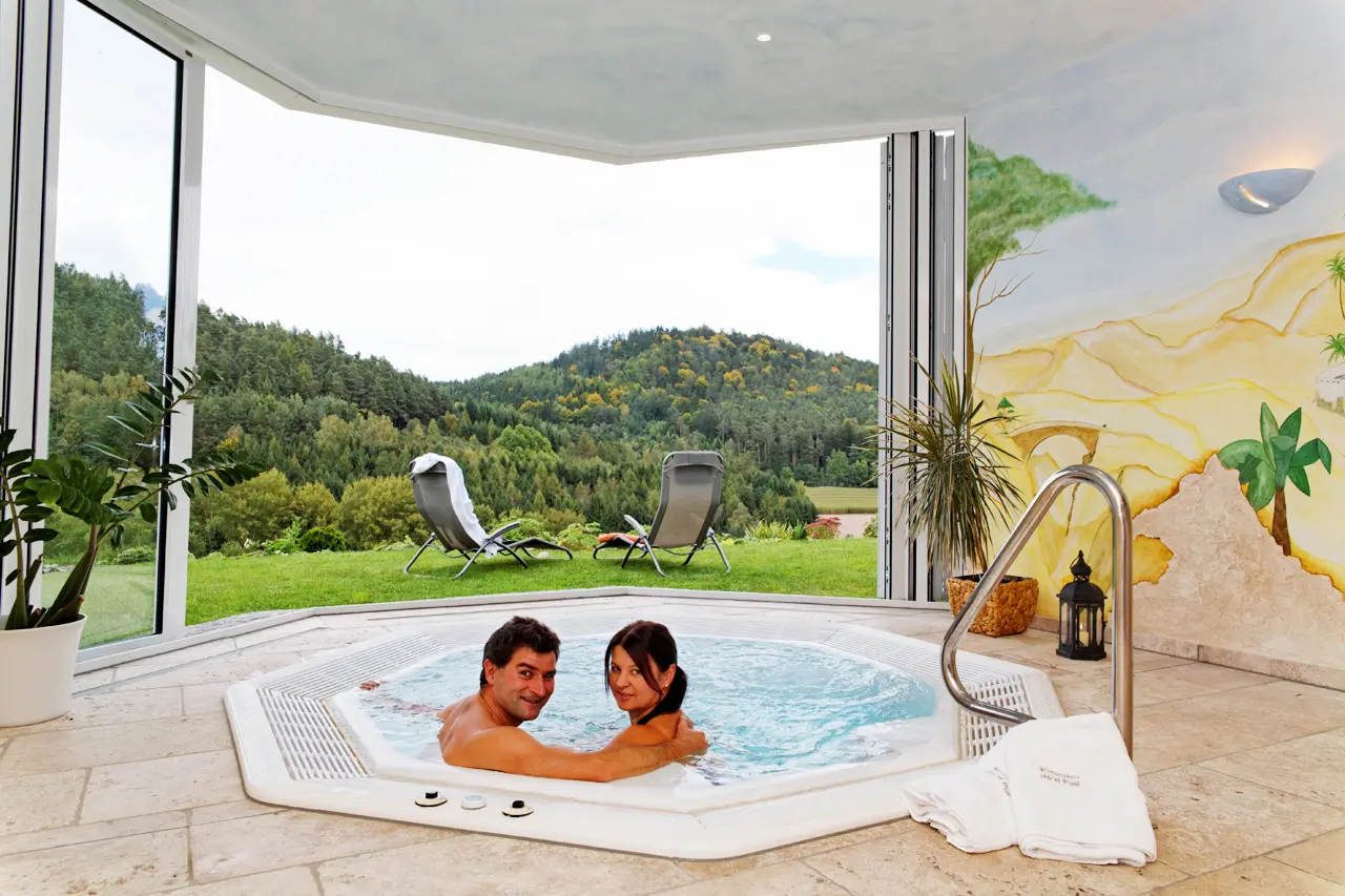 Paar entspannt im Whirlpool des Zedernhof Gesundheits- und Wellnesshotels mit Blick auf die grüne Natur und Berge.