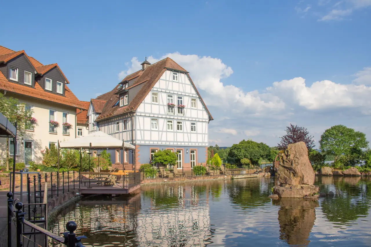 Idyllische Aussenansicht des Seehotel Niedernberg - Das Dorf am See mit Fachwerkhäusern am Ufer und Terrasse am Wasser.