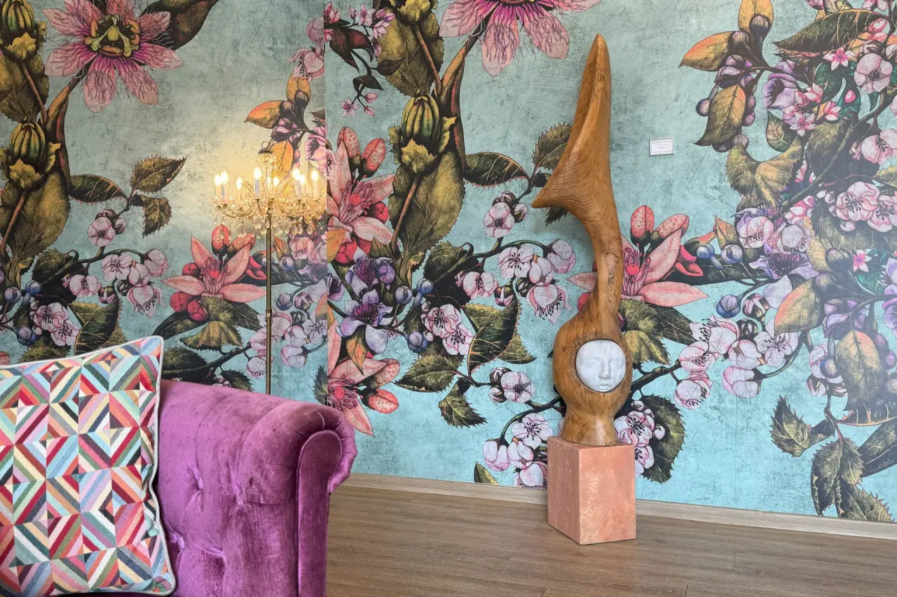 Detailansicht der farbenfrohen floralen Tapete, einer lila Samtcouch und einer Holzskulptur im Vitalhotel Sonneck.